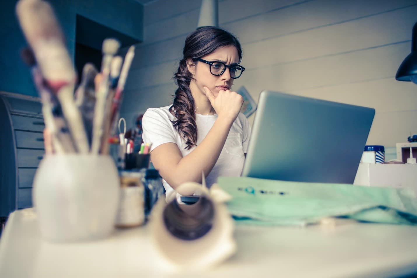 A woman in glasses is sitting at a desk with a laptop, seeking academic assistance.