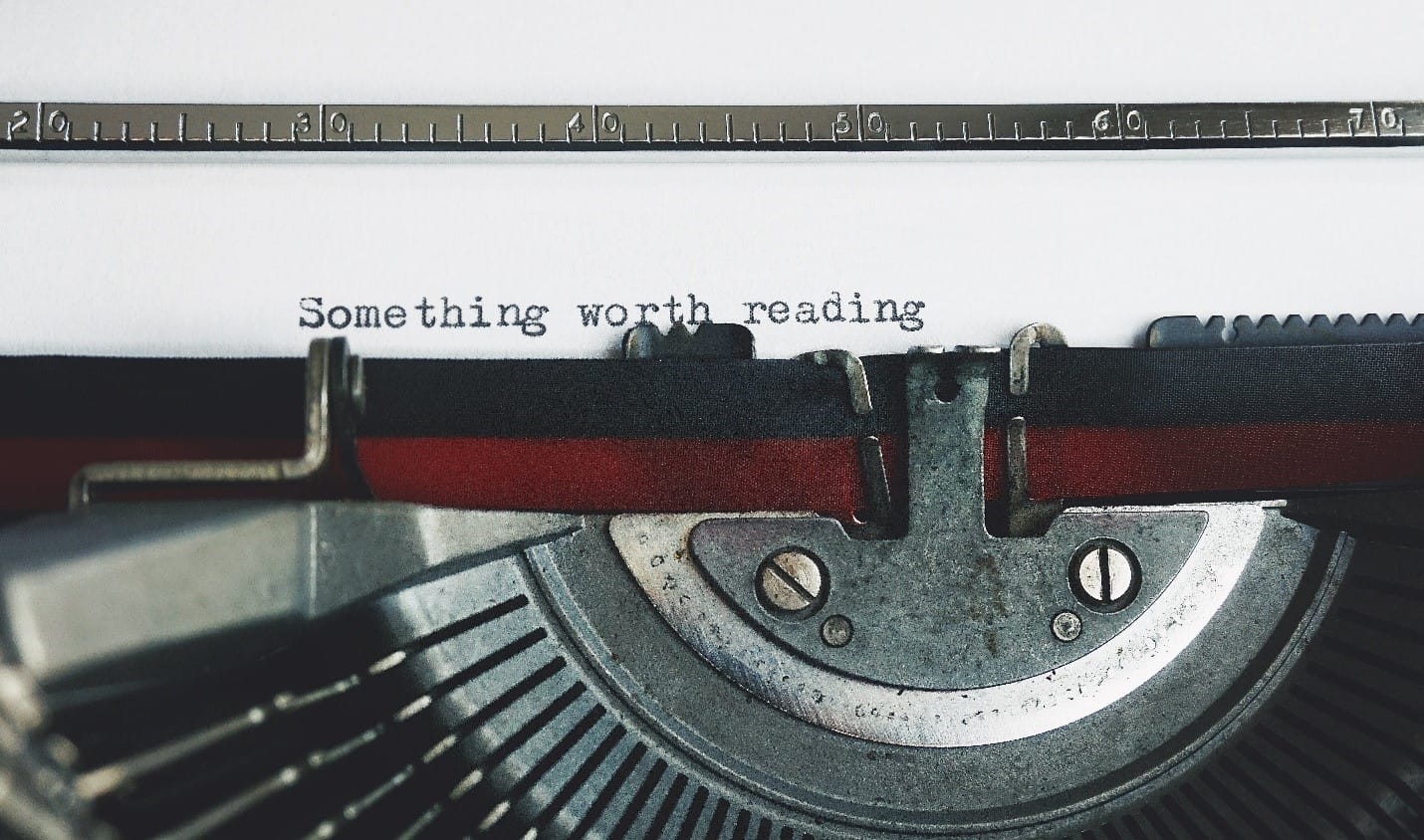 Vintage typewriter with a sheet of paper emerging, displaying the text "something worth reading." This image symbolizes the blog's purpose to guide readers in crafting effective essay outlines.