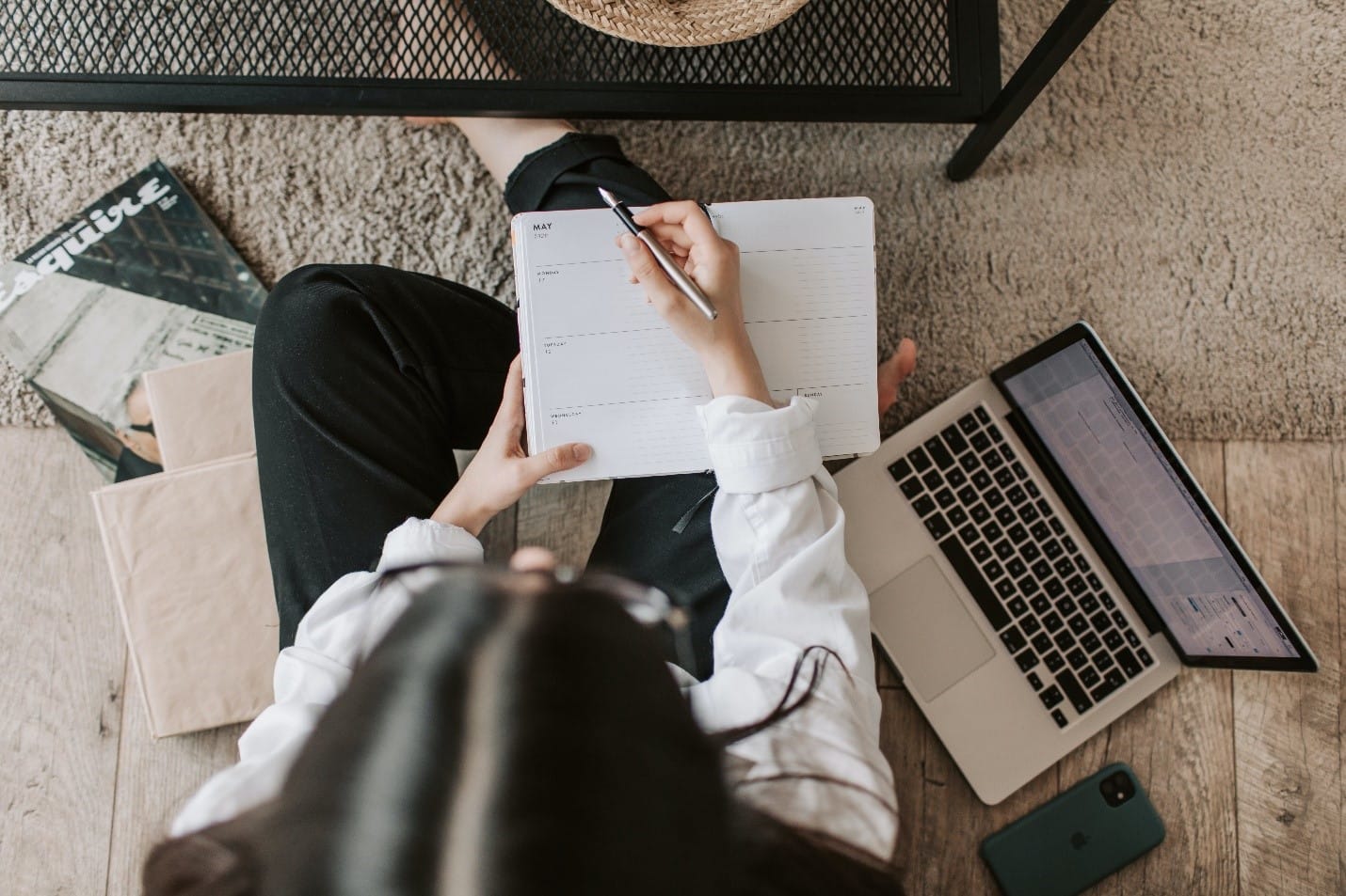 A woman at a desk, writing in a notebook and using a laptop is looking for strategies to start and finish her essay on a perfect note.