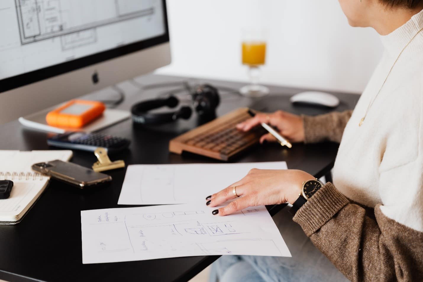A woman working at a desk with a laptop and papers working on her essay.