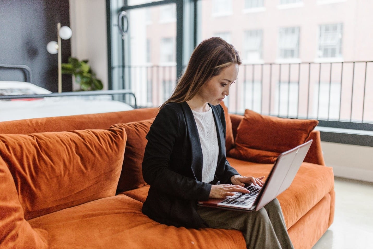 A woman, who struggles with argumentative writing, sits on a couch using a laptop.