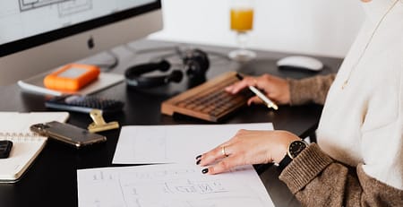A woman working at a desk with a laptop and papers working on her essay.