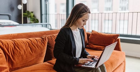 A woman, who struggles with argumentative writing, sits on a couch using a laptop.