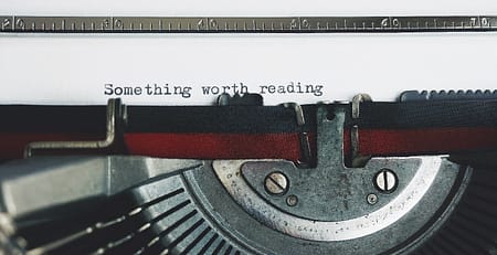 Vintage typewriter with a sheet of paper emerging, displaying the text "something worth reading." This image symbolizes the blog's purpose to guide readers in crafting effective essay outlines.