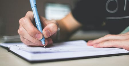 A young student writing essay in his notebook with a pen.