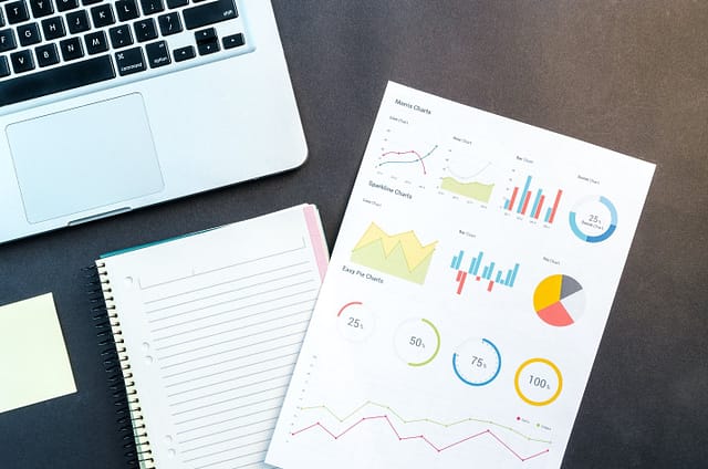 A notebook with statistical graphs on it and a laptop next to it.